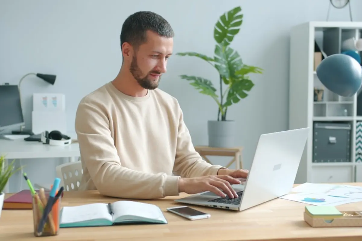 four people all on laptops, two men and two women, listen to person talking in a board meeting