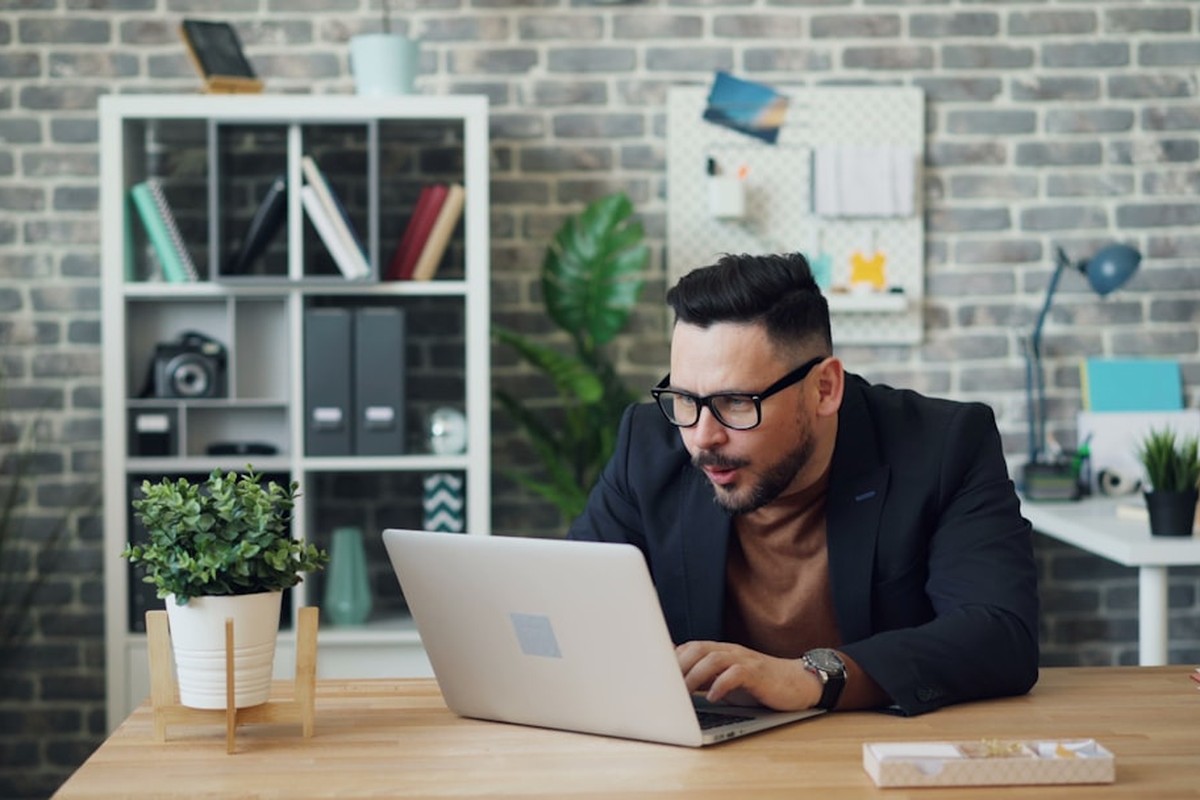 man standing and facing whiteboard with writings near woman pointing at it and facing man sitting beside table with laptop indoors