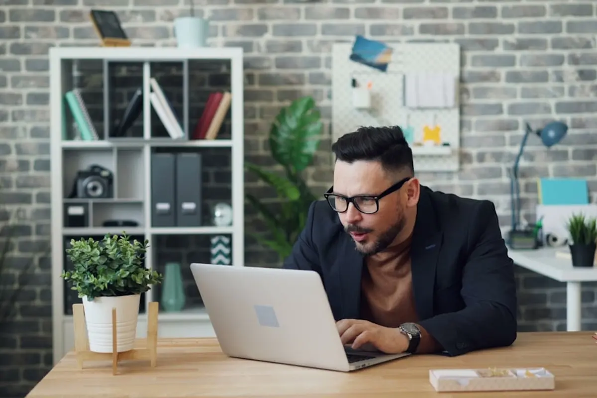 man standing and facing whiteboard with writings near woman pointing at it and facing man sitting beside table with laptop indoors