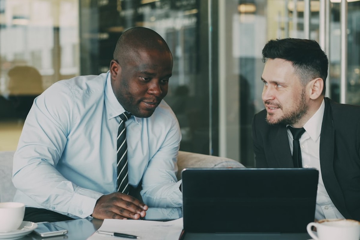 four people all on laptops, two men and two women, listen to person talking in a board meeting