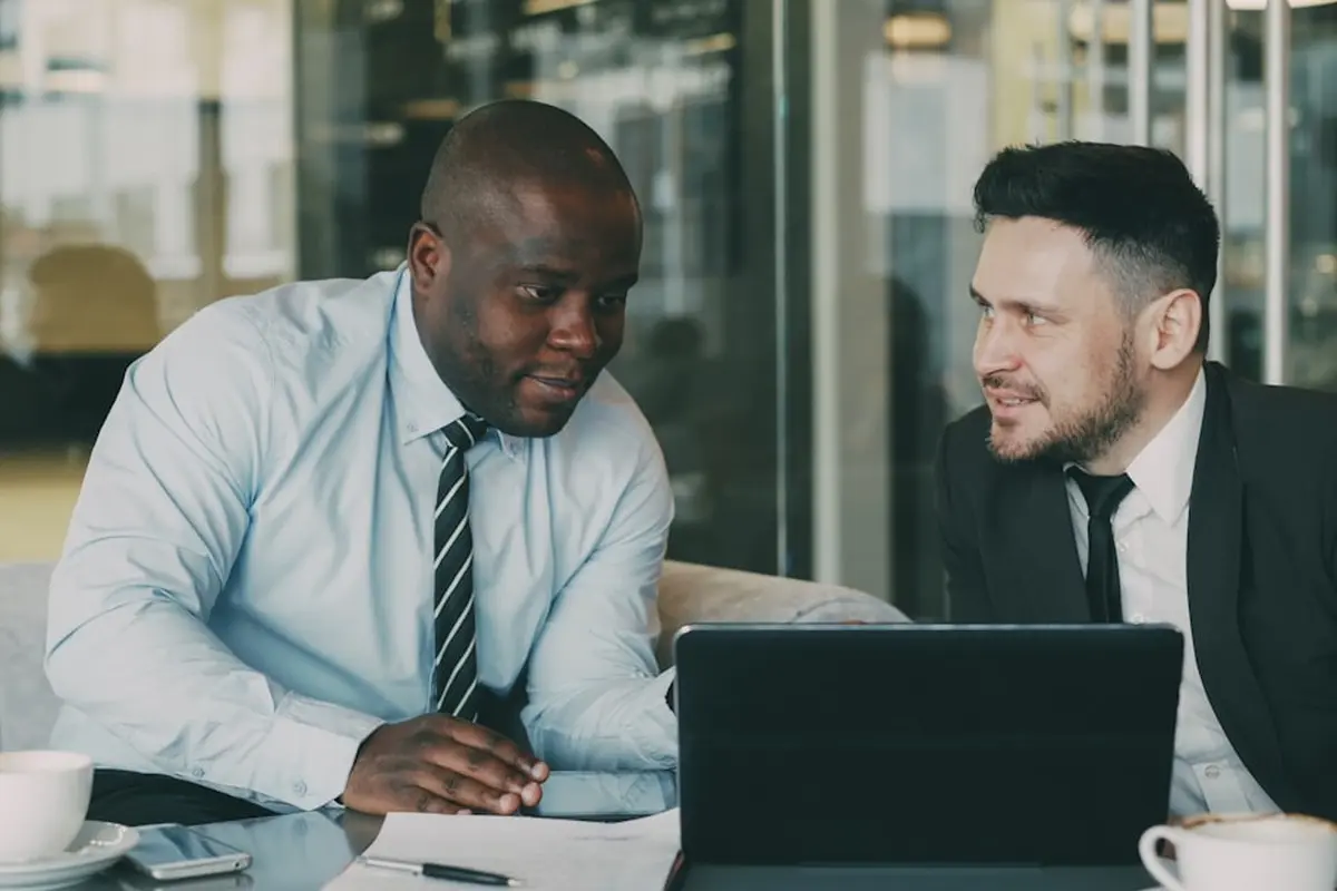 four people all on laptops, two men and two women, listen to person talking in a board meeting