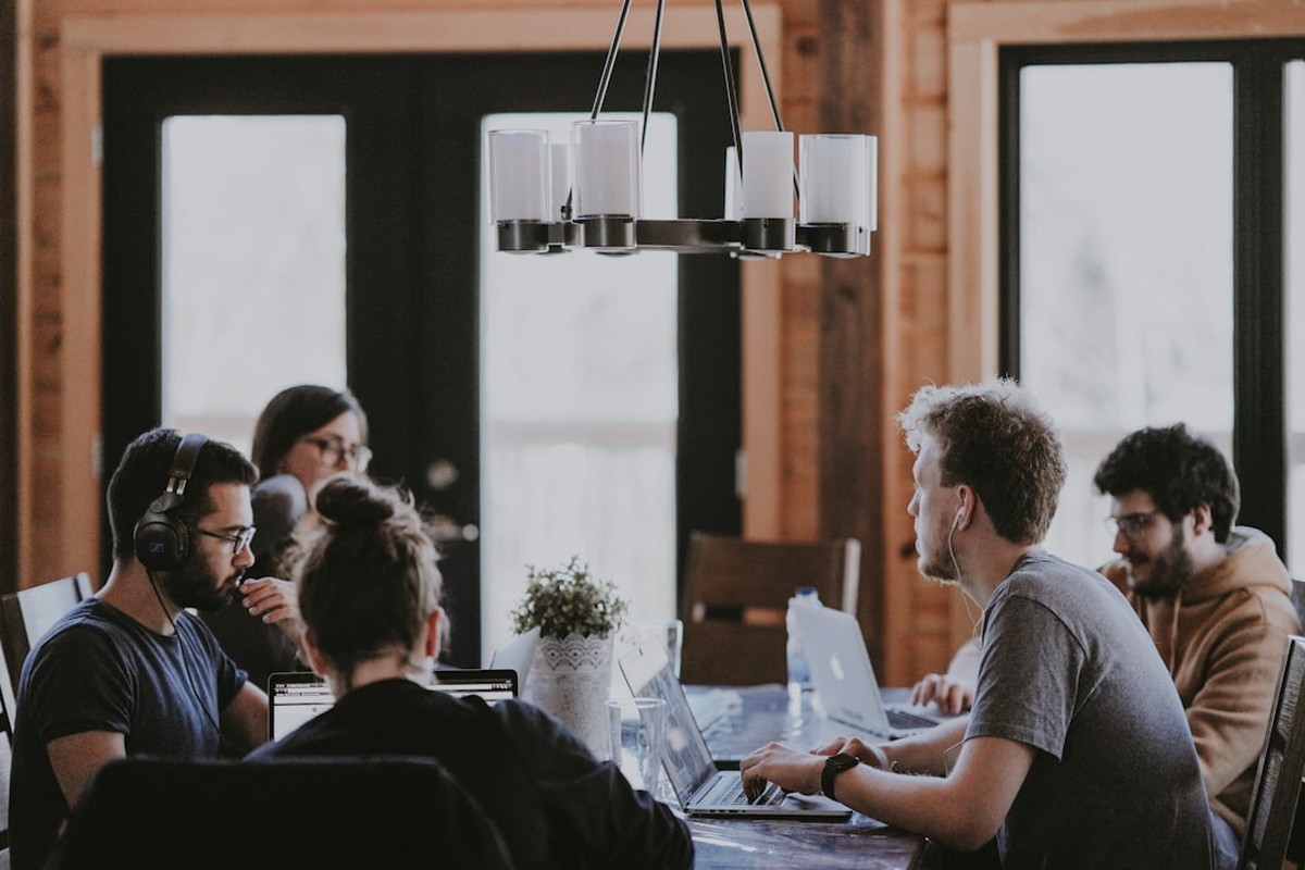 four people all on laptops, two men and two women, listen to person talking in a board meeting